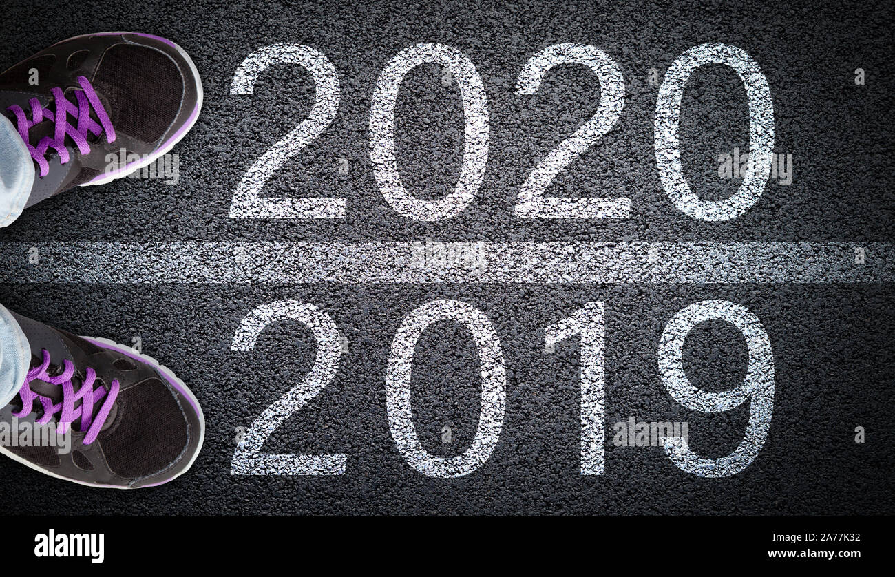 A teen girl in jeans and shoes standing on asphalt road between 2019 and New Year 2020. Concept of new beginning or directions in a new year ahead. Stock Photo
