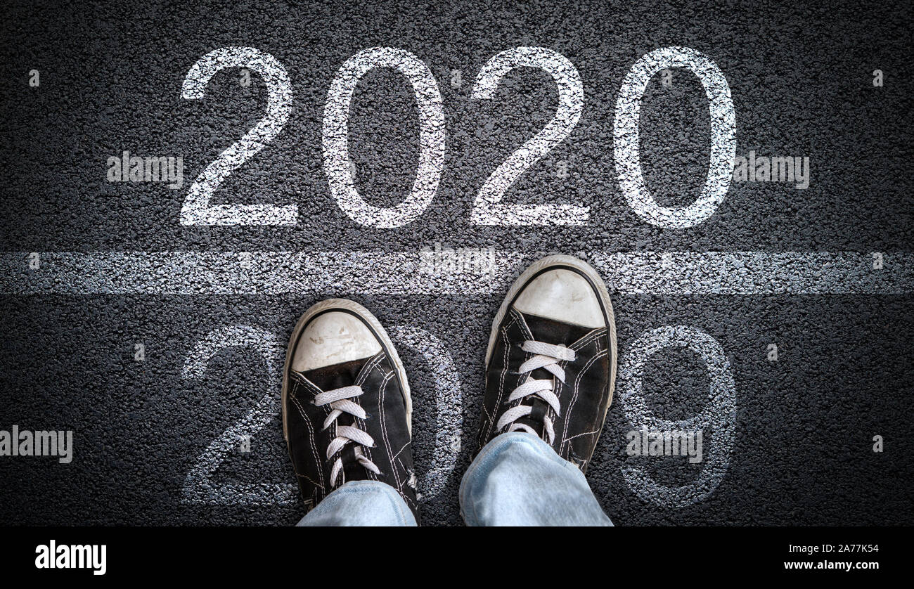 A teenager in jeans and canvas shoes standing on asphalt road ready to step from 2019 into New Year 2020. Concept of new beginning or directions in a Stock Photo