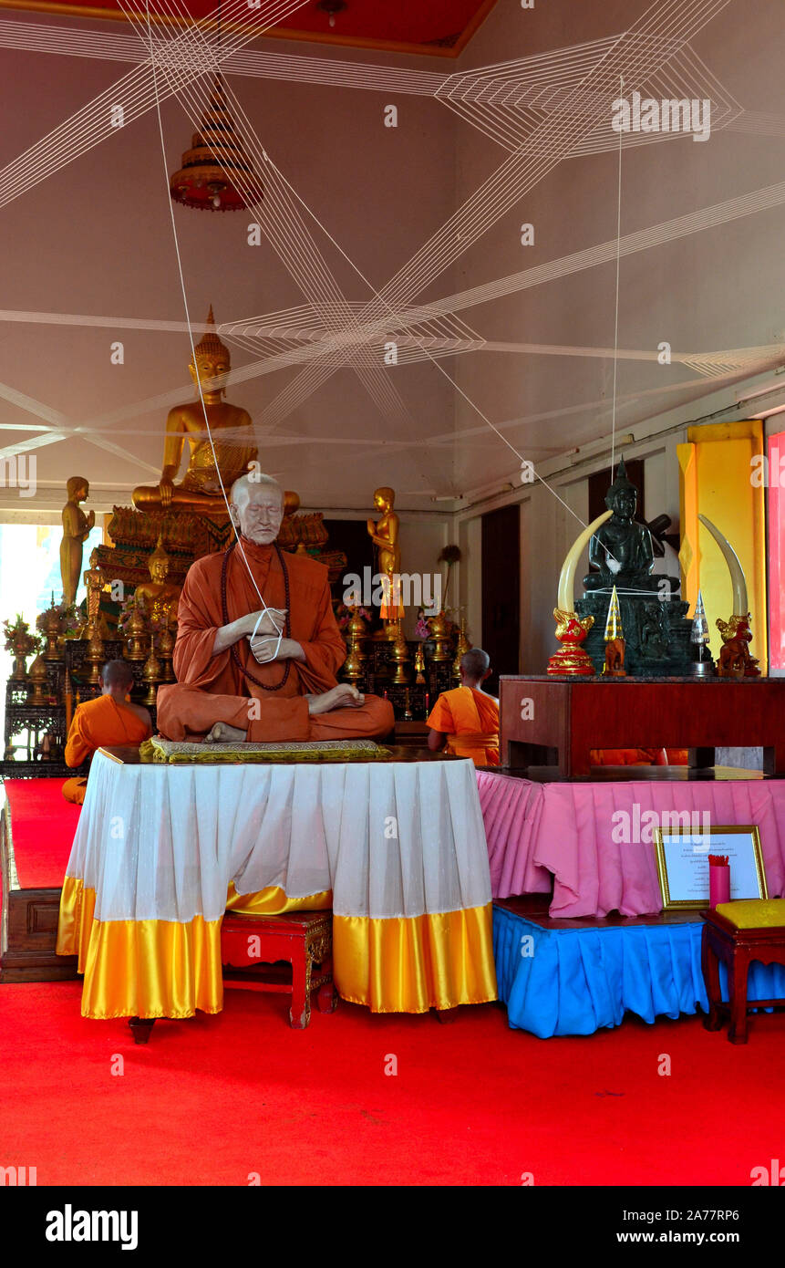 Two monks praying in front of a wax sculpture of another monk with ...