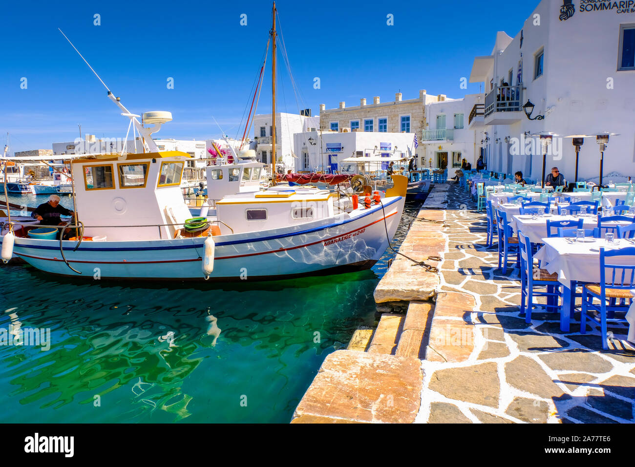 Fishboat and restaurant tables on the harbour. Naoussa village. Paros island. Cyclades islands. Greece. Stock Photo