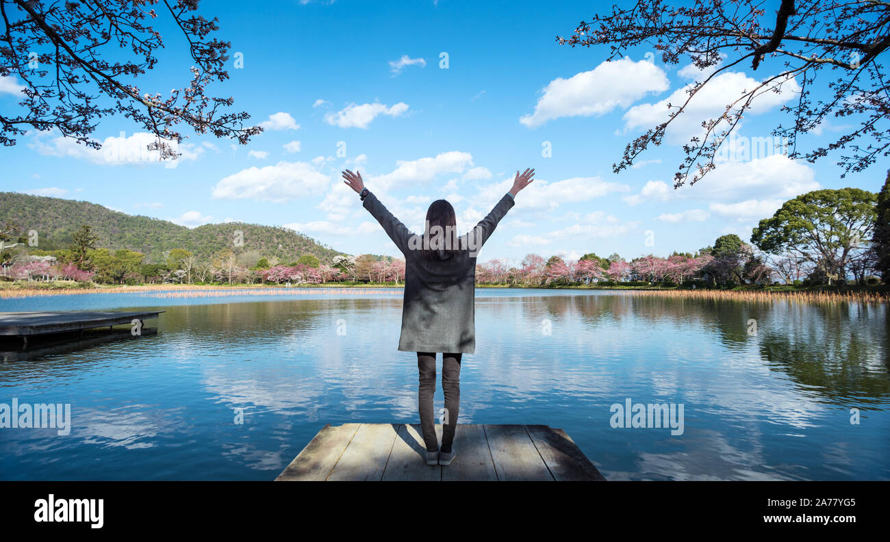 Young woman enjoying freedom with open hands in front of lake with nature landscape during spring time Stock Photo
