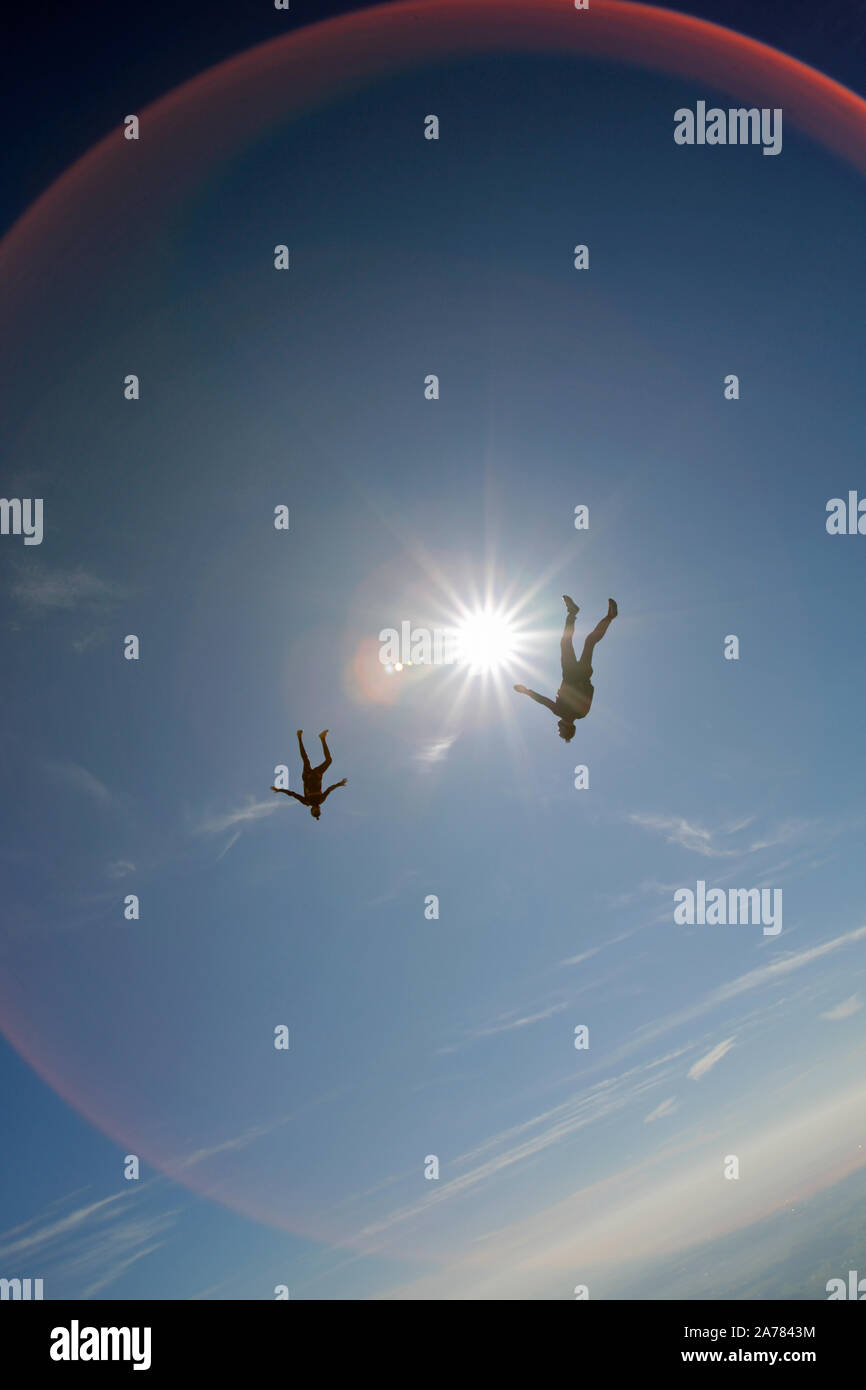 These two skydivers are flying high in the blue sky around each other and playing hard to catch hands. Each diver has fun and a big smile on his face. Stock Photo