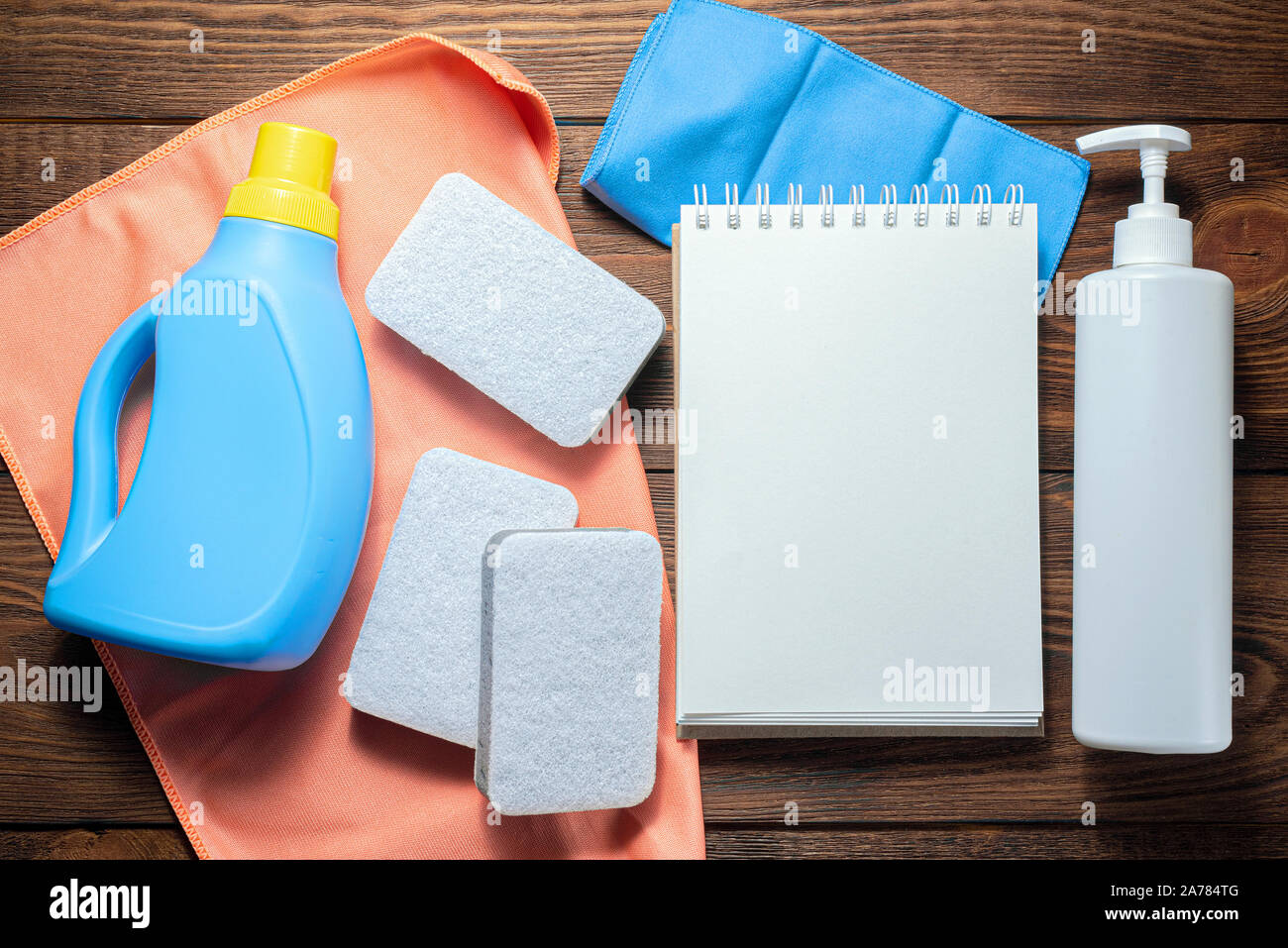 Washing supply, softener, detergent, dish cloth and blank page notepad on wooden table. Household tips mock up. Stock Photo