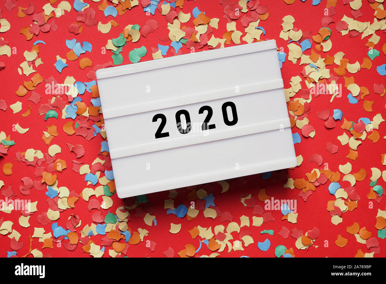 year 2020 lightbox sign on red paper background with confetti - new years eve party celebration concept flat lay Stock Photo