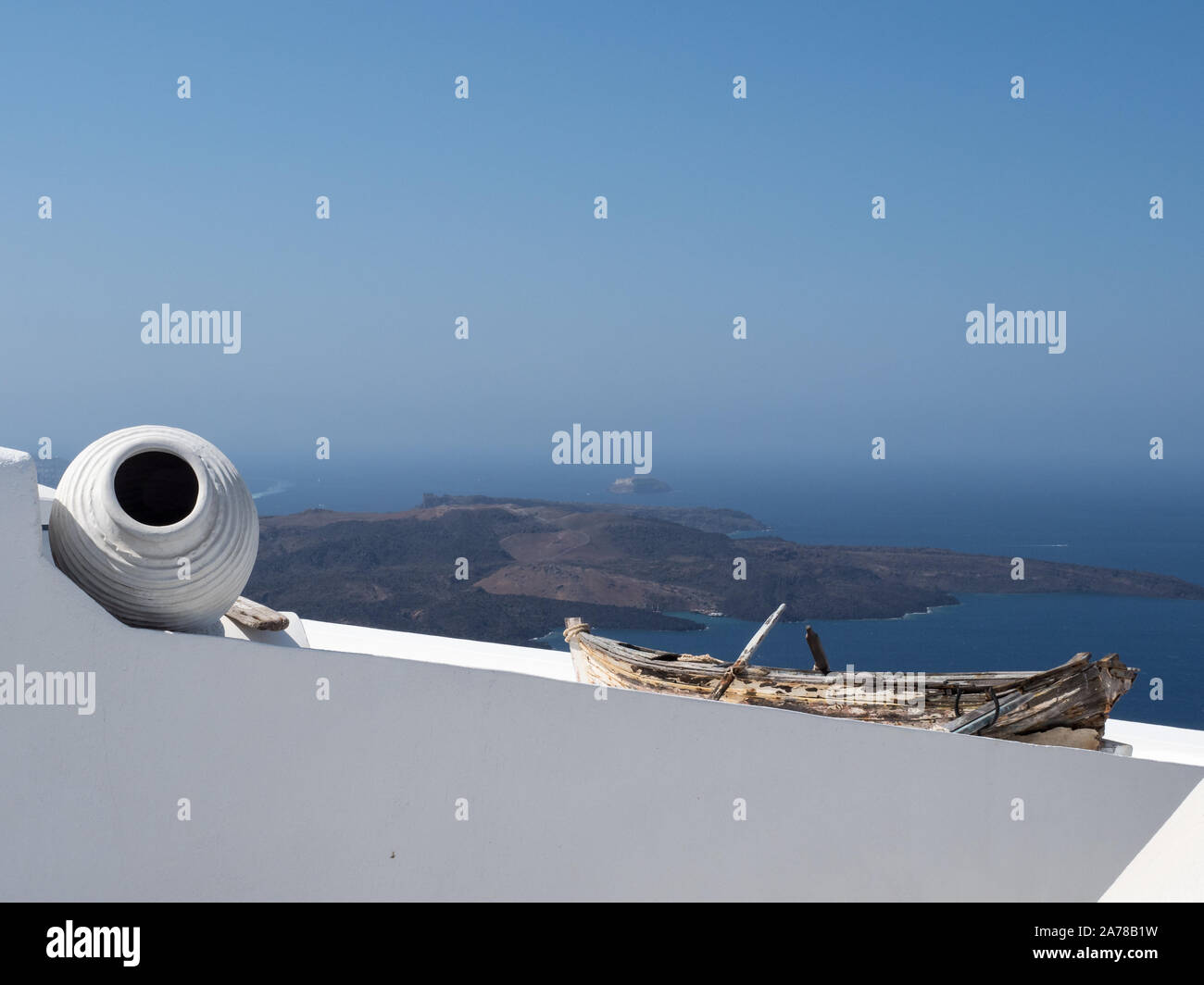 a view of vase pot salvaged, repurposed rowing boat on top a white wall distant mountains sea blue sky horizon Fira Santorini Stock Photo