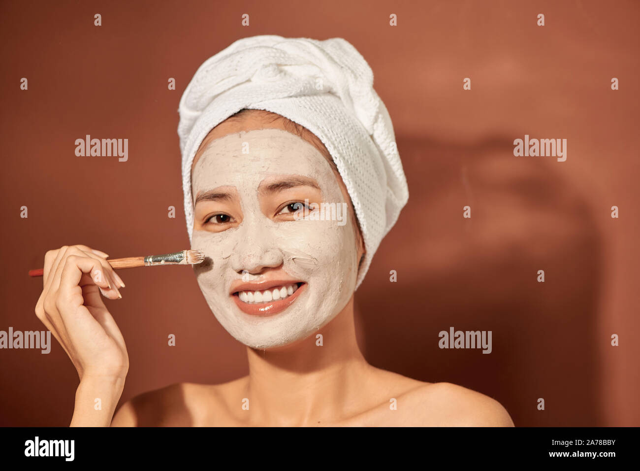 Beautiful Asian woman applying facial mask on her face. Skin care and treatment, spa, natural beauty and cosmetology concept. Stock Photo