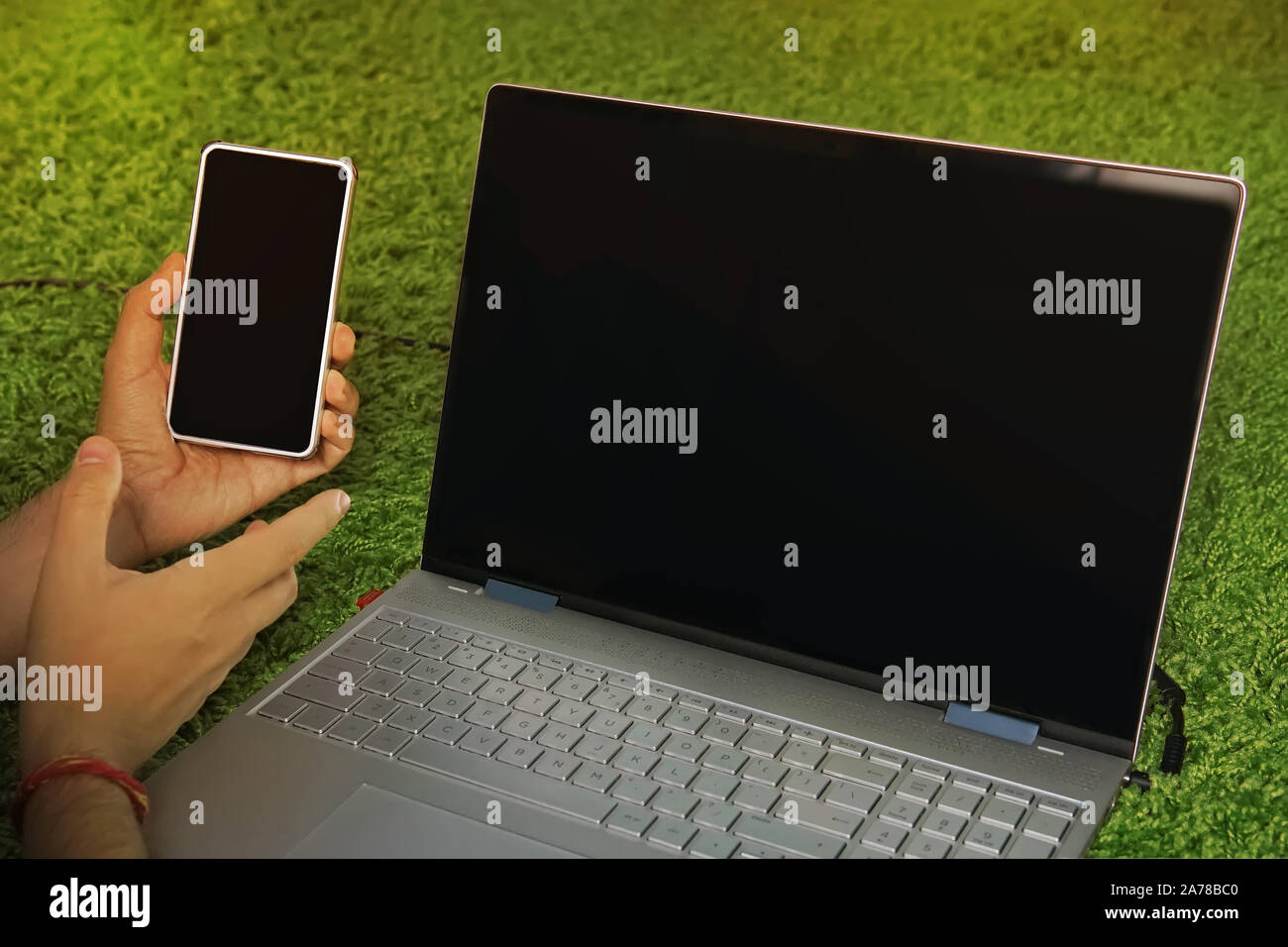 Man holds the smartphone with black screen lying on the carpet near the black-screened laptop. Digital devices for domestic internet access. Usage of Stock Photo