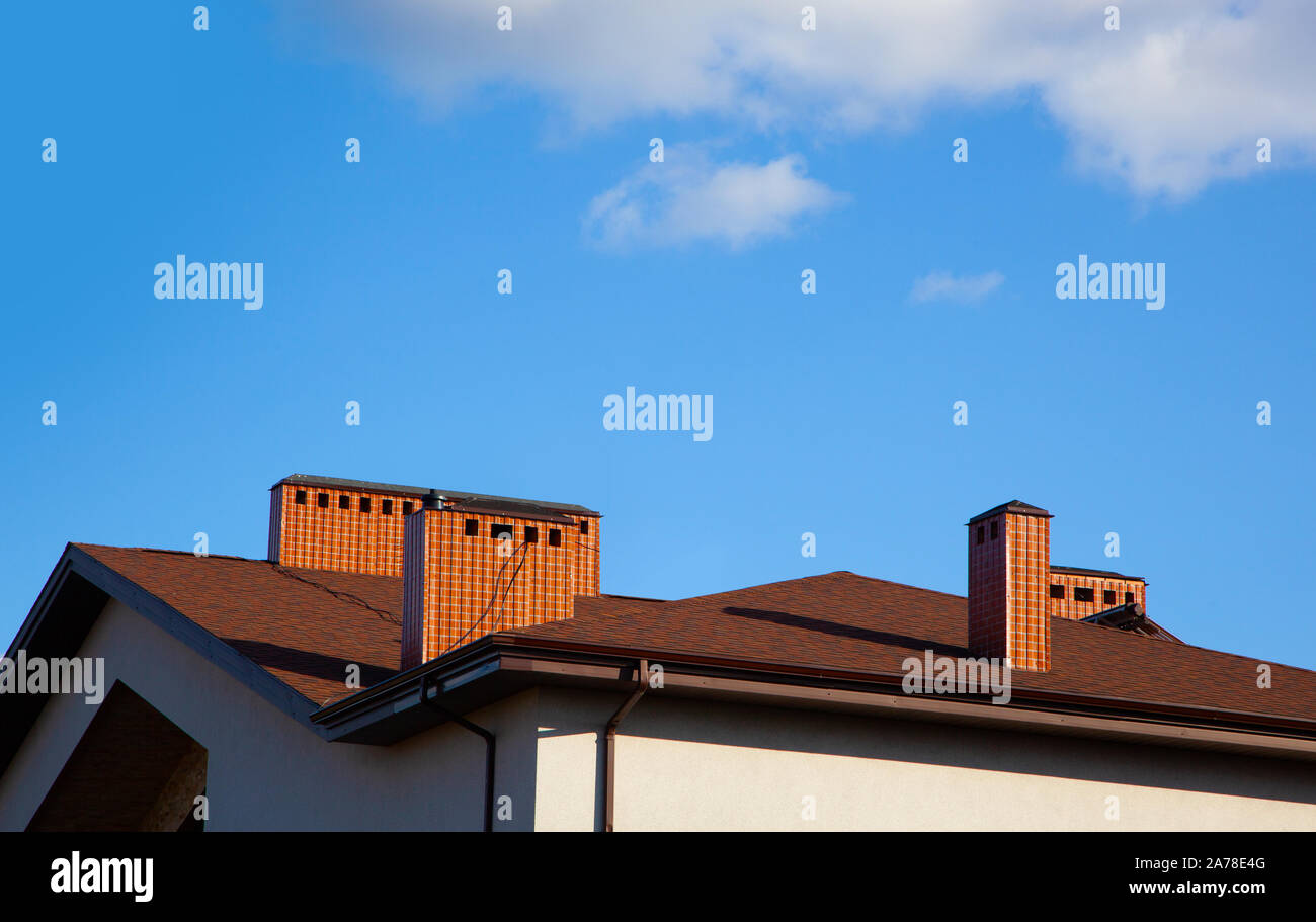 House with brick chimney in bright sunlight, against a deep blue sky ...