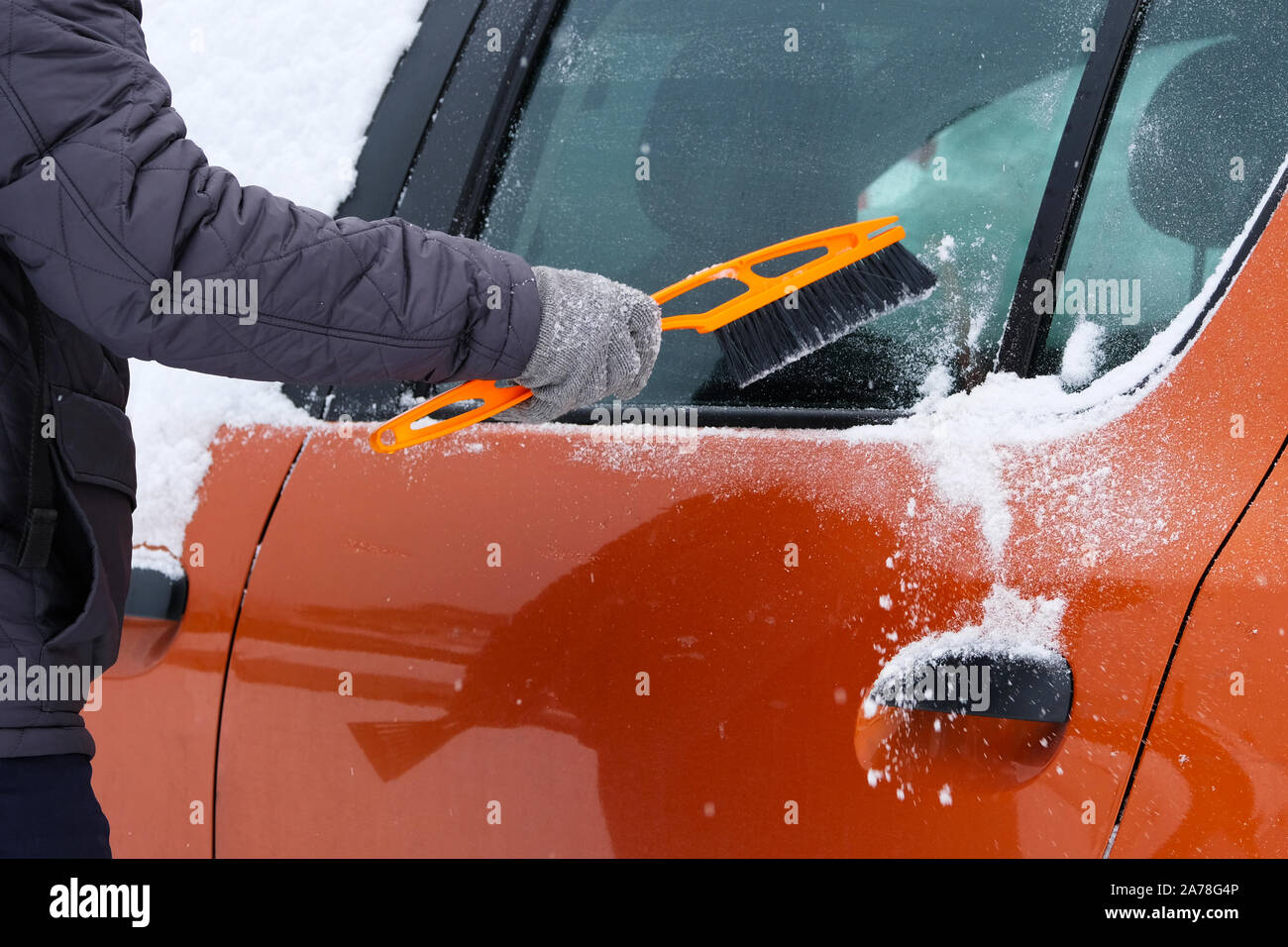 Car covered with snow. Man brushing and shoveling snow off car after snow storm. Brush in mans hand. Stock Photo