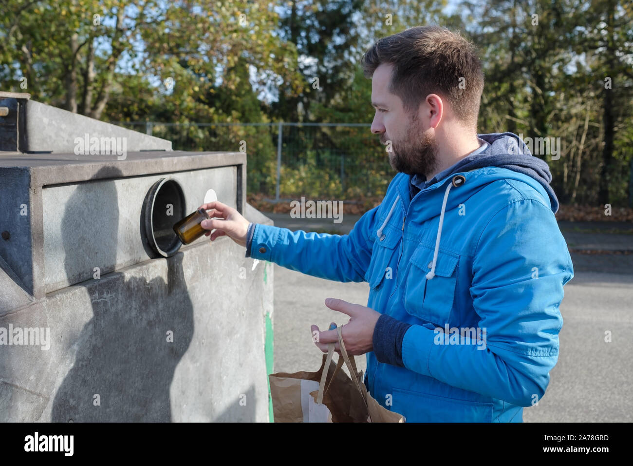 Young caucasian man in blue coat throwing away glass jar into a