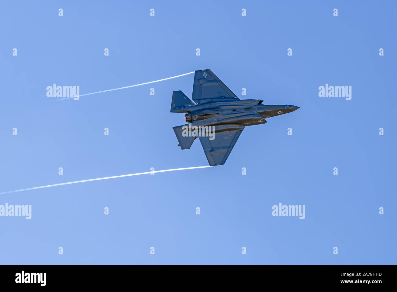 Lockheed Martin F-35c Lightning II flying in clear sky with afterburner and vapor off wingtips Stock Photo