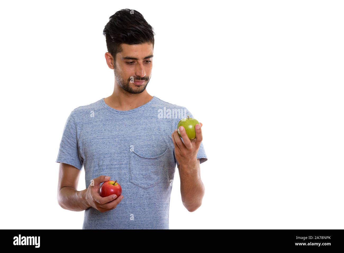 Studio shot of young Persian man holding red apple and green apple ...