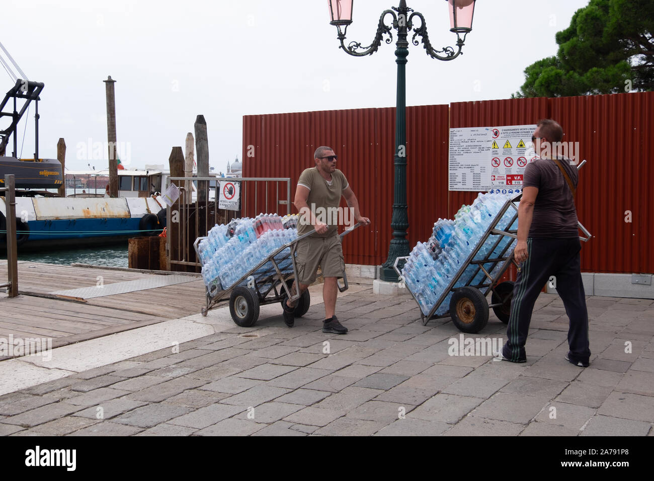 Two men pulling hugely loaded two wheeled trollies, holding packs of