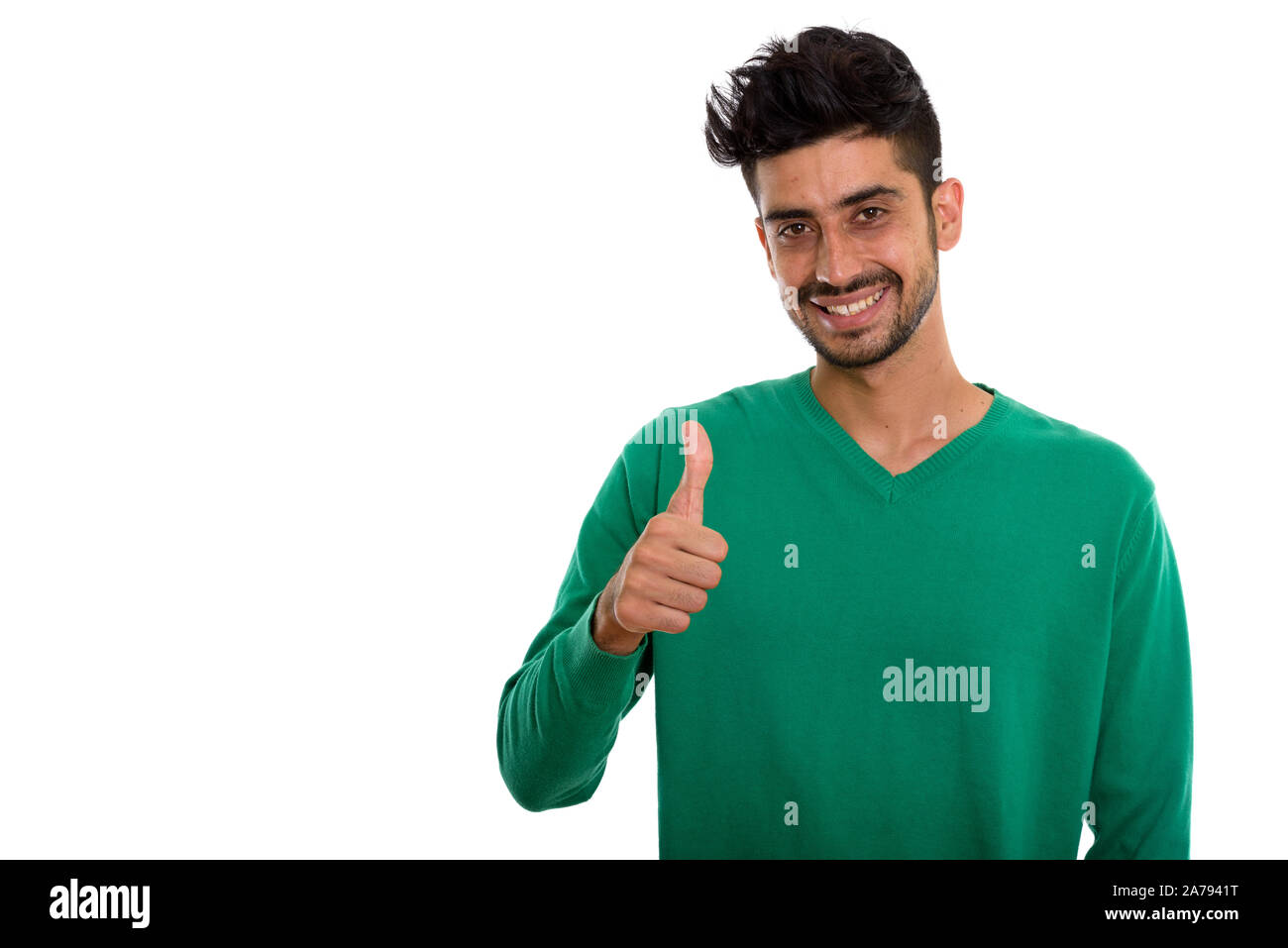 Studio shot of young happy Persian man smiling while giving thum Stock Photo