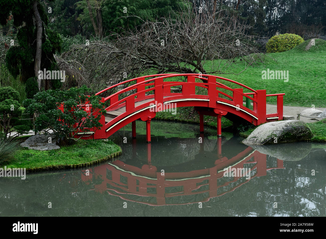 a view of a red bridge above an artificial lake at Pierre Baudis Japanese Garden, a Japanese style public park, in Toulouse, France Stock Photo
