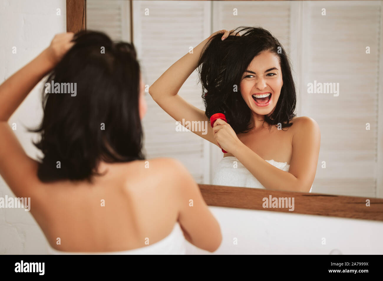 young happy woman brushing healthy hair in front of the mirror. girl combing her hair and fools around Stock Photo