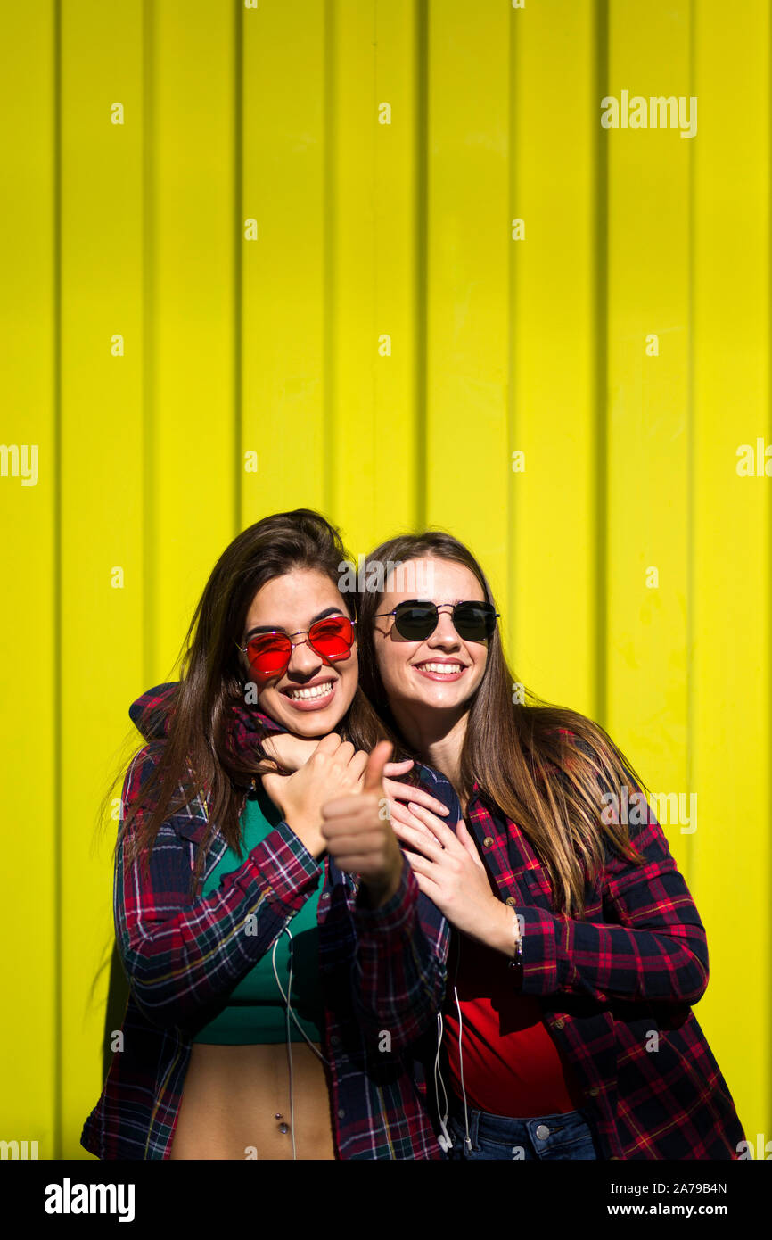 Image of two young happy women friends standing outdoor over yellow wall Stock Photo