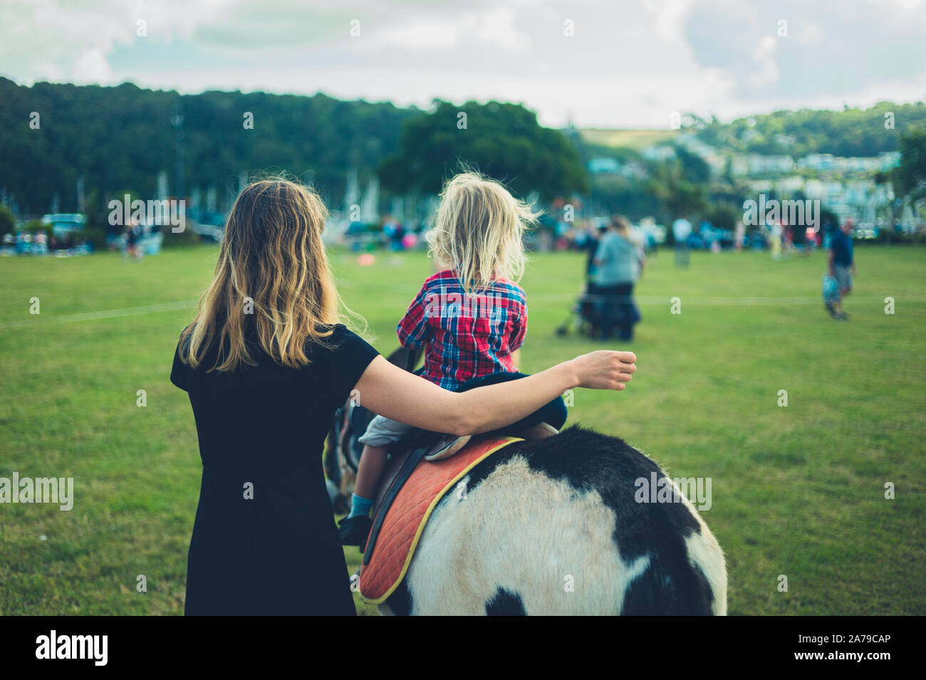 A little toddler is riding a donkey at the fair with his mother walking ...