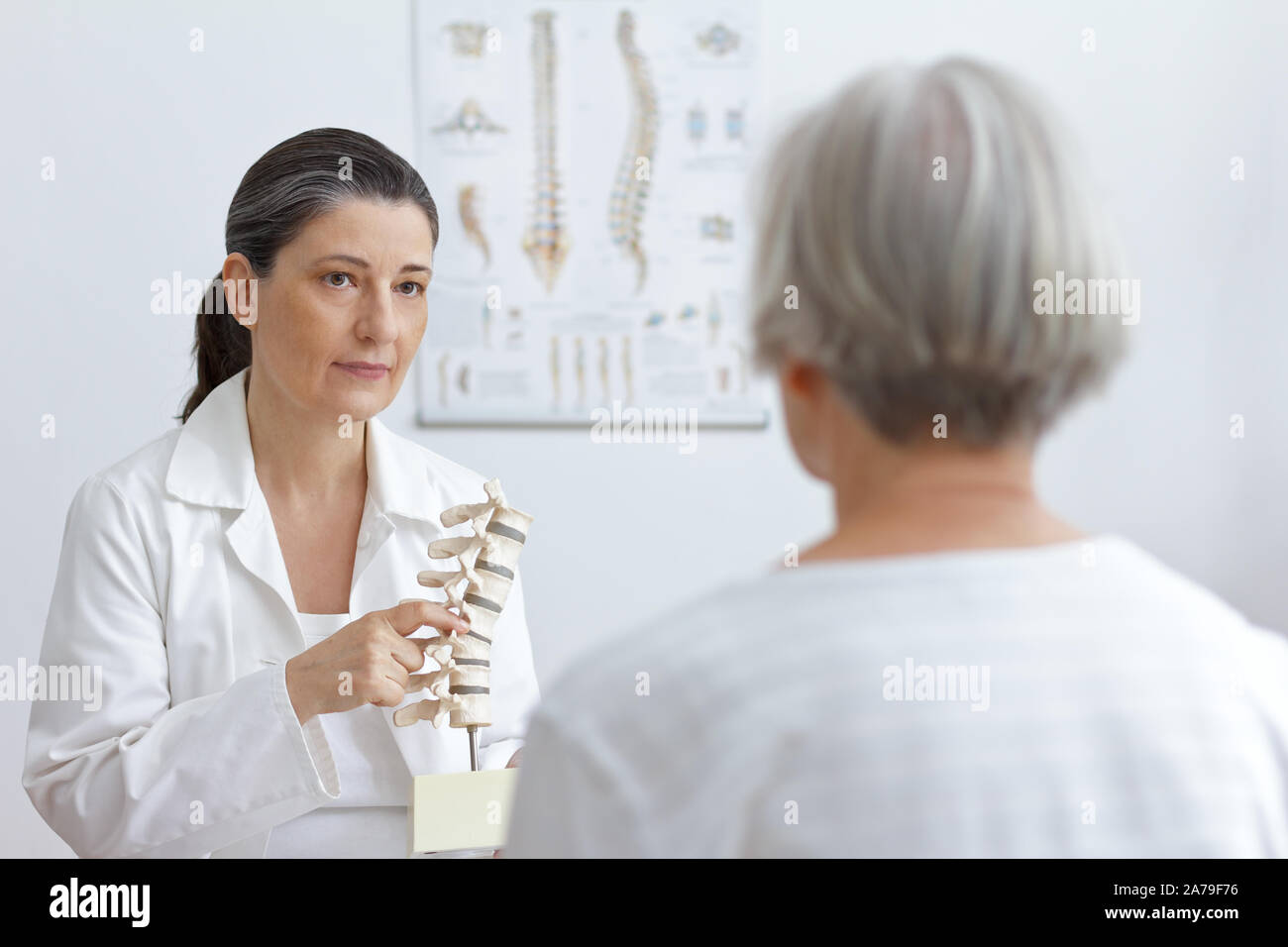 Aging and back pain concept: doctor of orthopedics showing her senior patient a slipped disk on a backbone model. Stock Photo