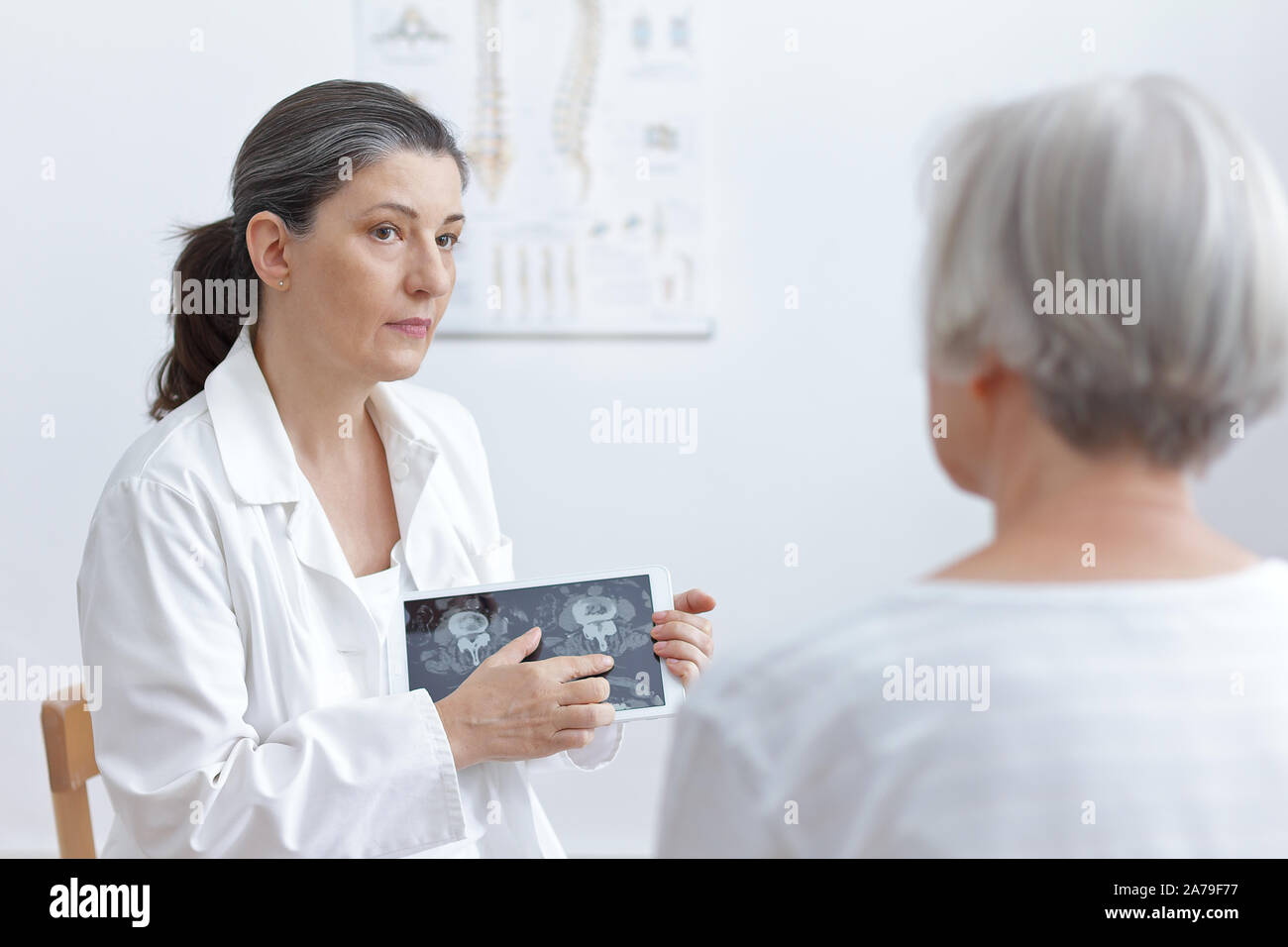Female doctor with tablet computer showing her senior patient cat scan images of her degenerated vertebrae. Stock Photo