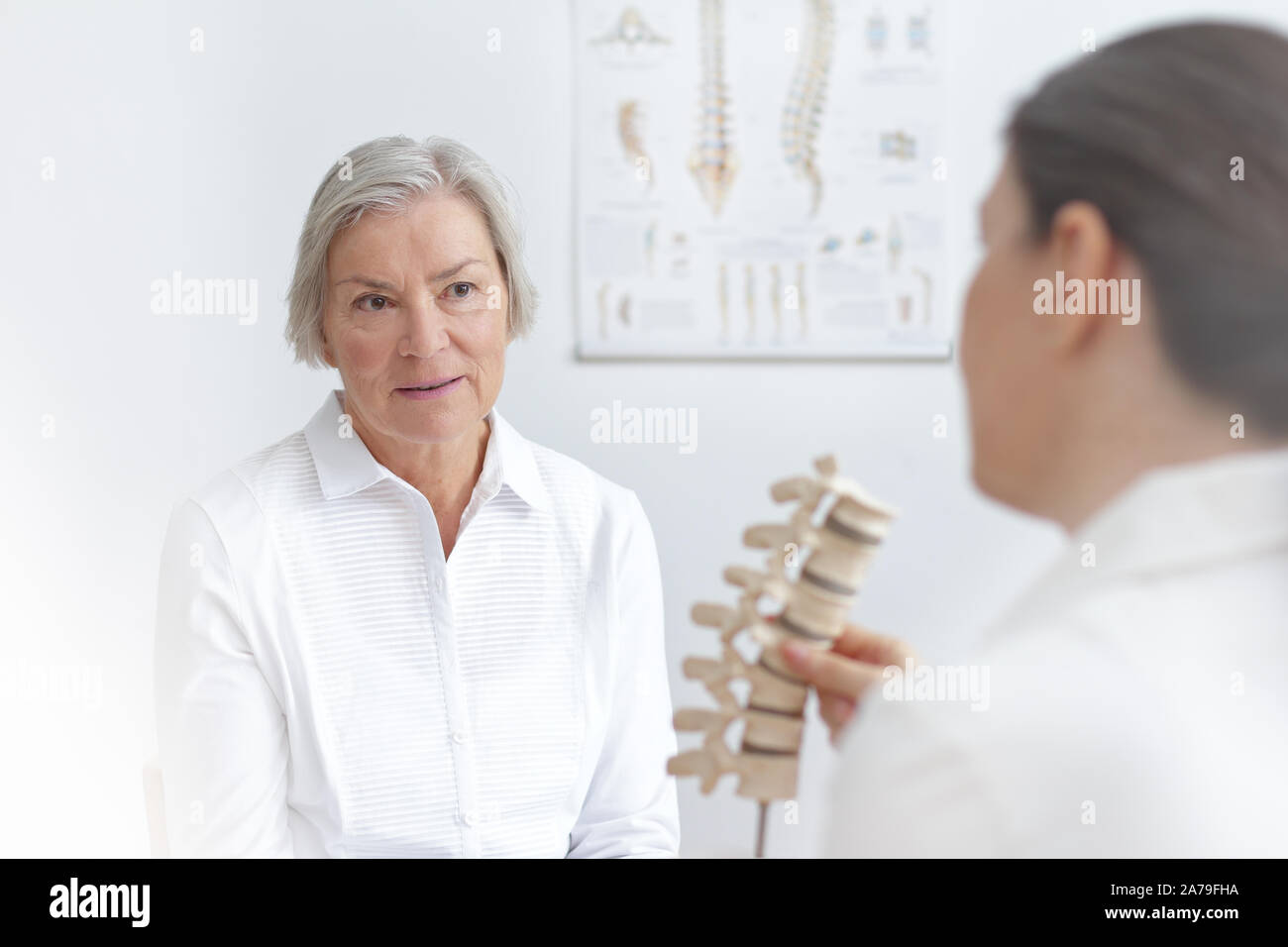 Aging and back pain concept: doctor of rheumatolgy showing her senior patient a slipped disk on a backbone model. Stock Photo