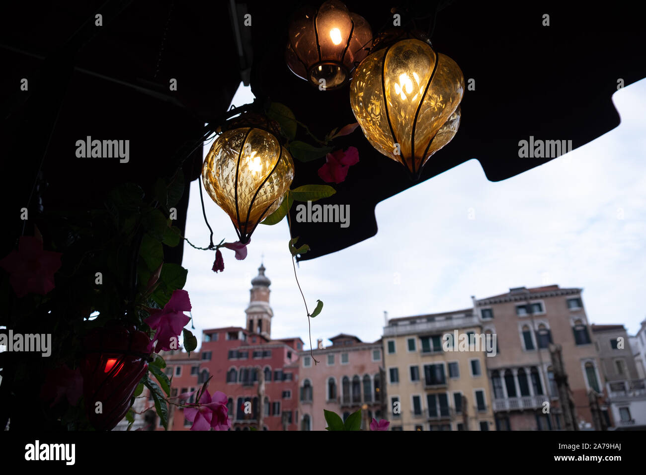 Evening view from a restaurant at the edge of the Grand Canal by Rialto bridge framed by lit strings of multi shaped and coloured glass lanterns. Stock Photo