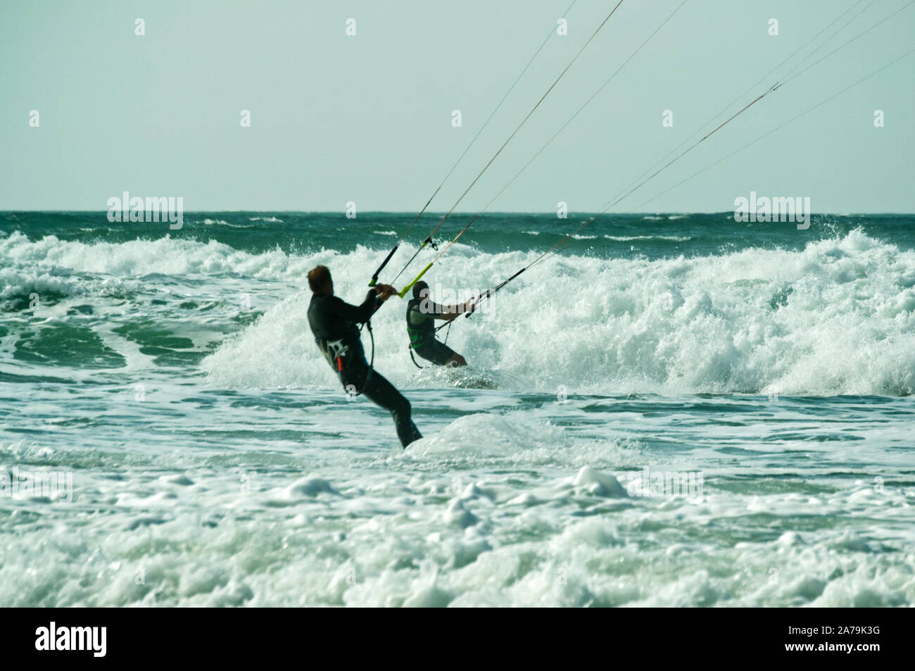 A pair of kite surfers in rough seas driving through breaking waves close to the beach on the Atlantic coast, France Stock Photo