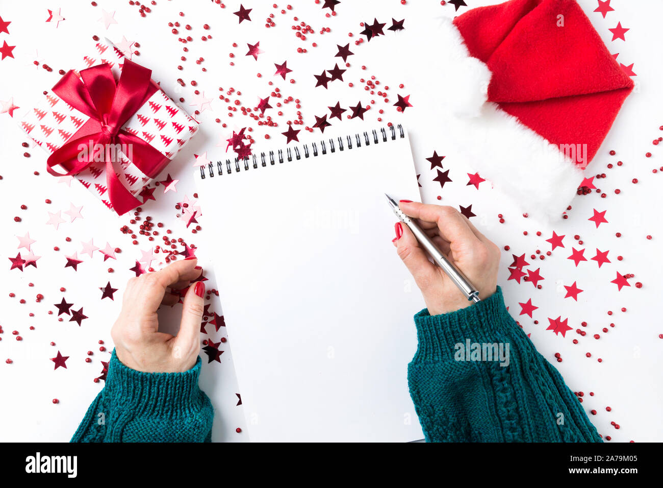 Woman in green sweater writes checklist of plans and dreams for next year. Wish list for Christmas and New Year. To Do List for New 2020 year with red Stock Photo
