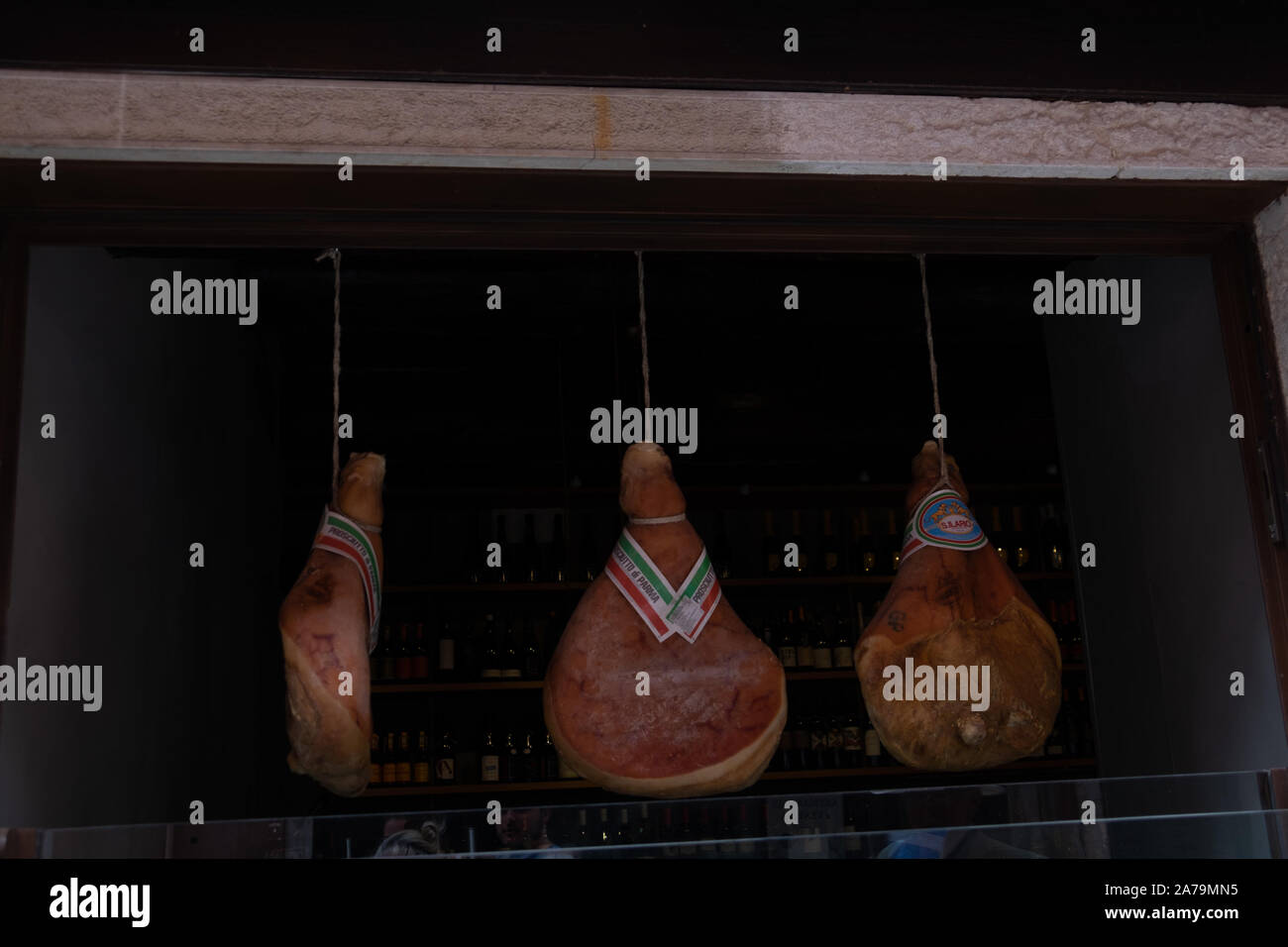Three specialist and traditionally cured whole hams, hanging on ropes suspended from a wooden beam to the open aired front of a Venetian shop. Stock Photo