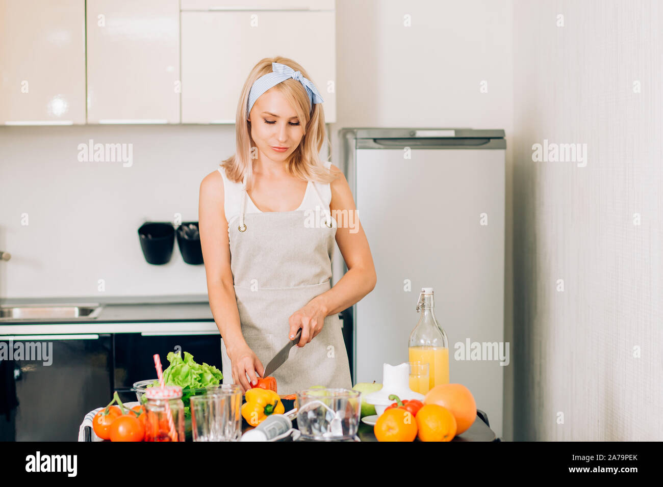 https://c8.alamy.com/comp/2A79PEK/healthy-food-diet-concept-lovely-european-blonde-woman-in-apron-with-headband-cooking-vegetable-salad-for-dinner-cutting-tomatoes-on-chopping-boa-2A79PEK.jpg