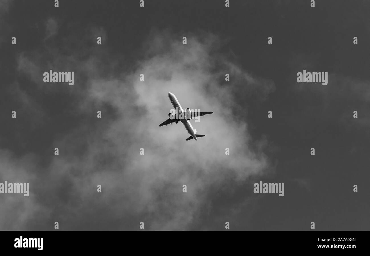 A black and white picture of an airplace flying overhead. Stock Photo