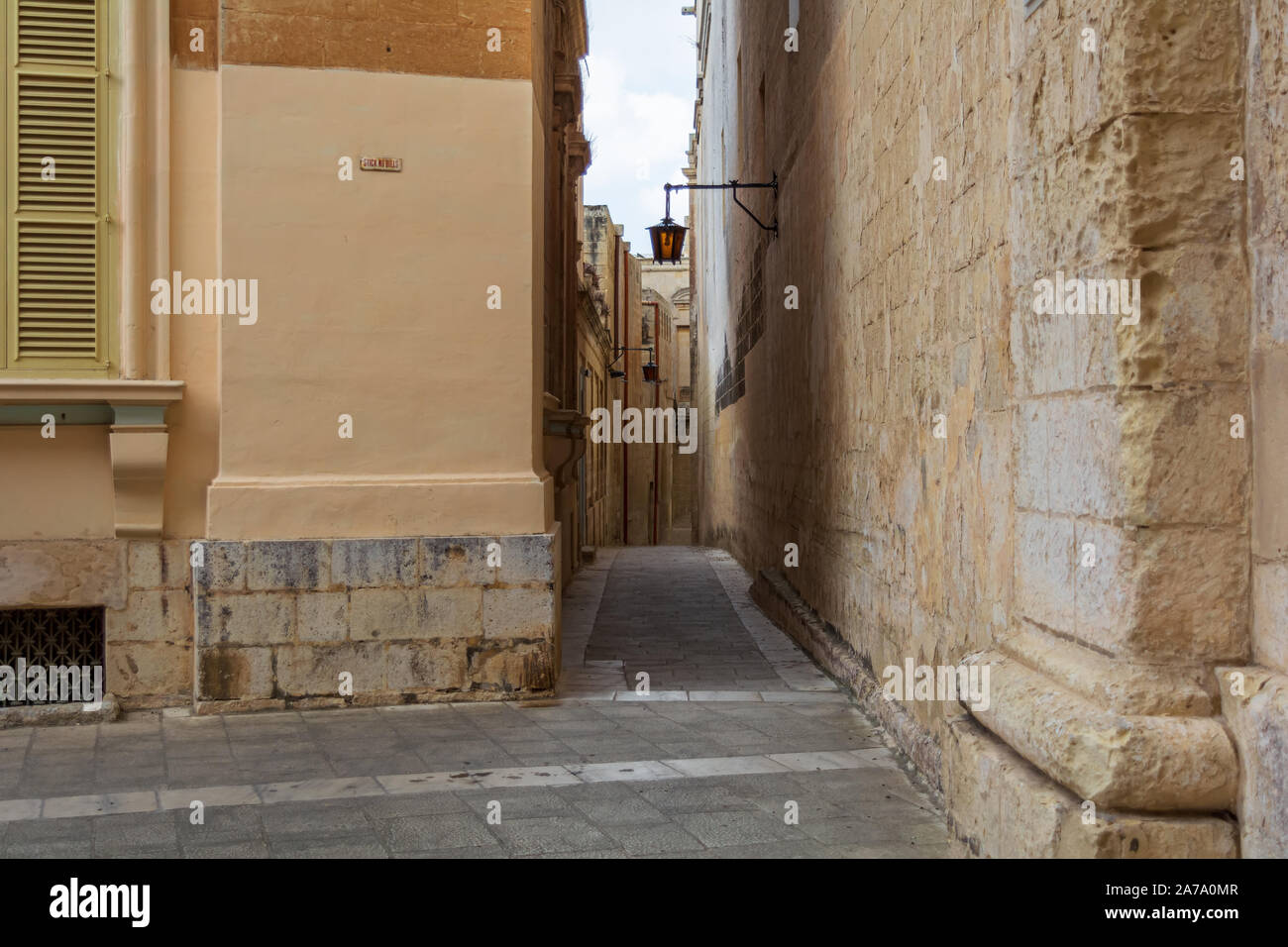 Typical Mdina street. Narrow medieval street of Mdina, also known as 'Silent city', paved with stone slabs and surrounded with yellow limestone walls, Stock Photo