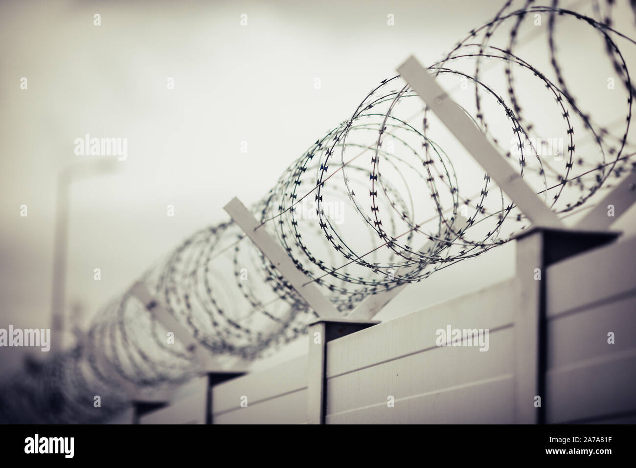 Shallow depth of field (selective focus) and filtered image with a razor wire on the outside wall of a governmental institution on a cloudy day. Stock Photo