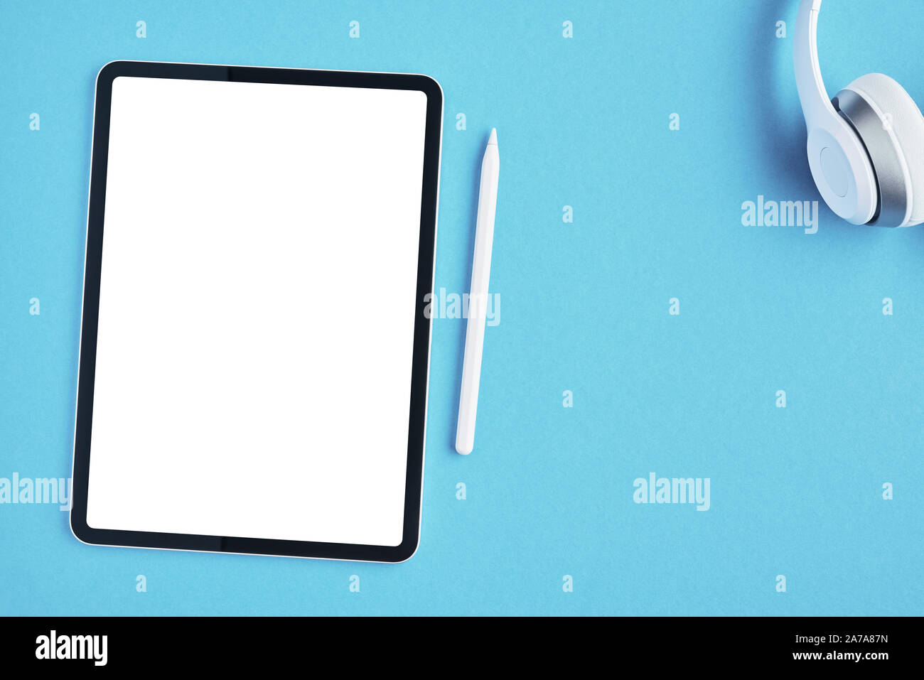 Tablet mockup with white pencil and white wireless headphones on blue background. Top view. Copy space. Stock Photo