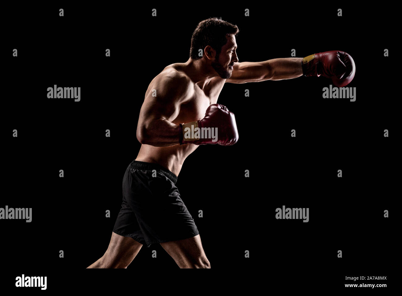 Strong muscular man with boxing gloves throwing a punch over a black