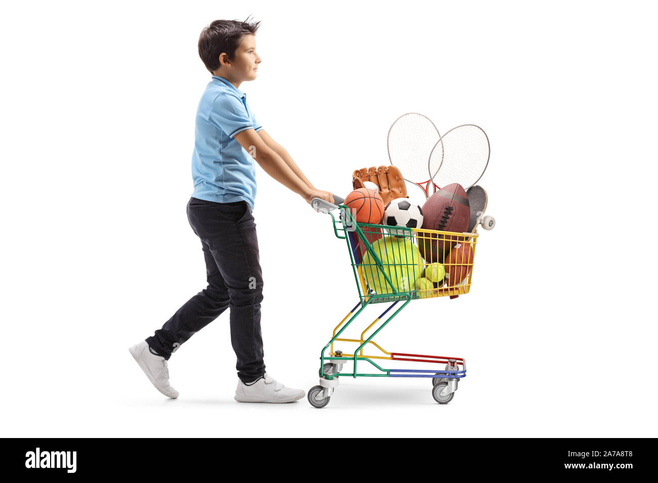 Full length profile shot of a boy walking and pushing a mini cart with sport items isolated on white background Stock Photo