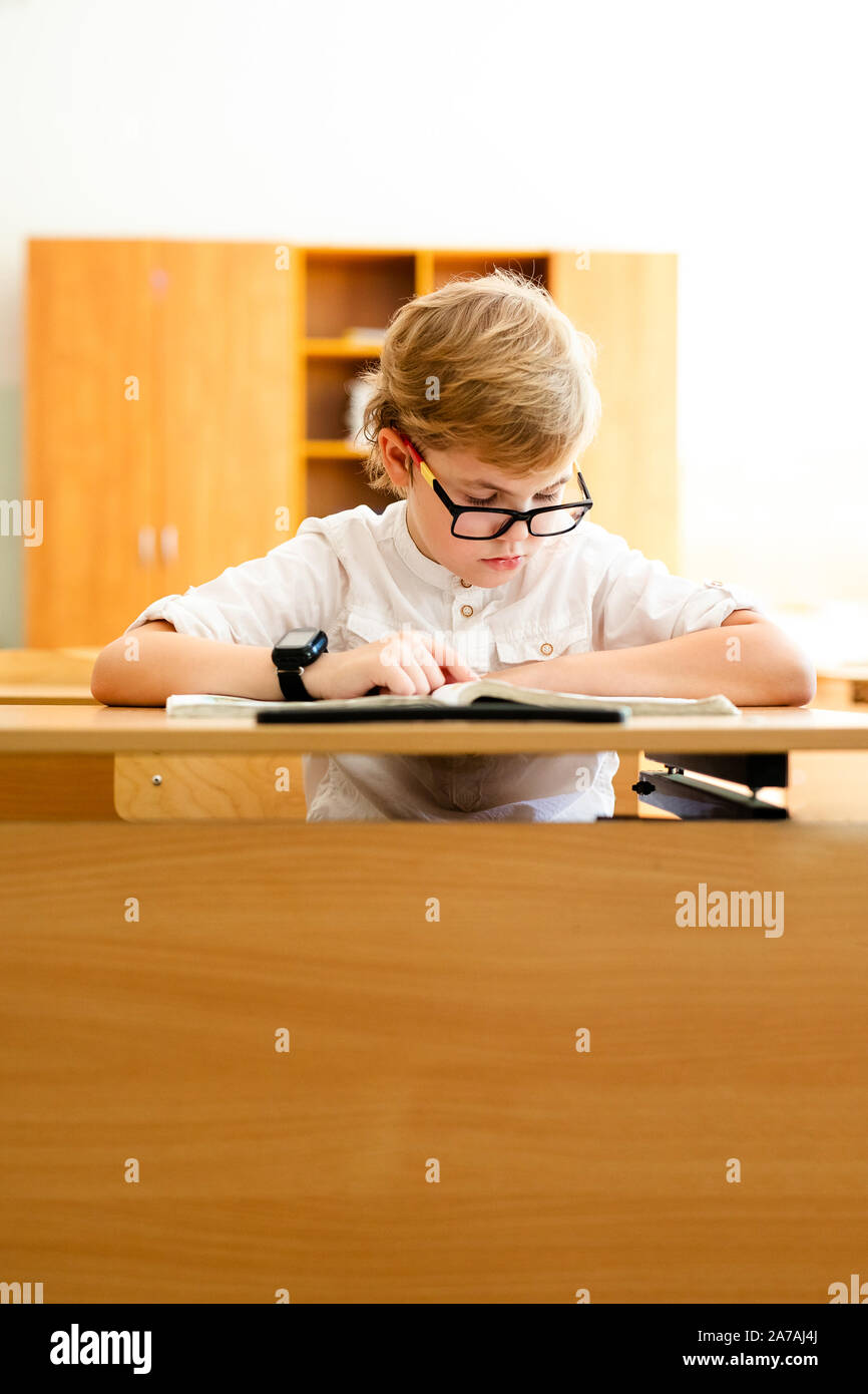 Elementary school student with black glasses writing maths answer on chalkboard. Stock Photo
