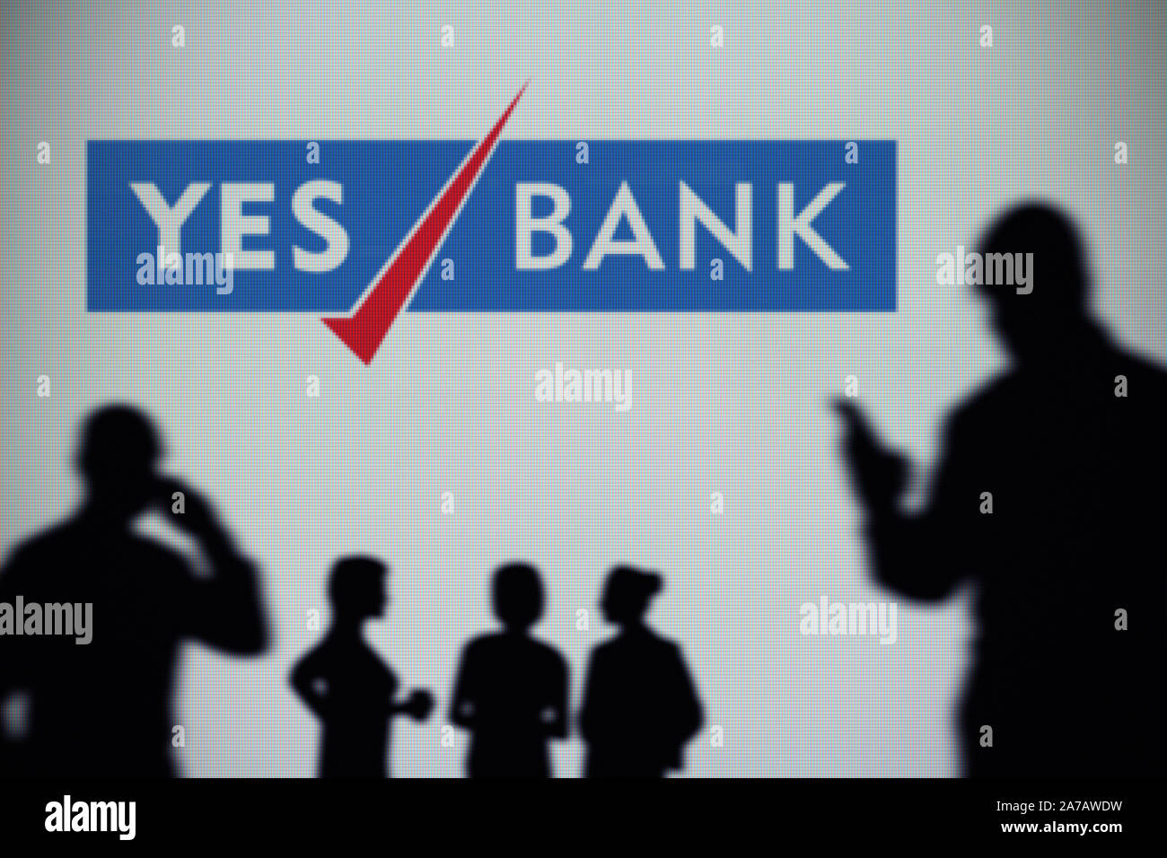 The Yes Bank logo is seen on an LED screen in the background while a silhouetted person uses a smartphone (Editorial use only) Stock Photo