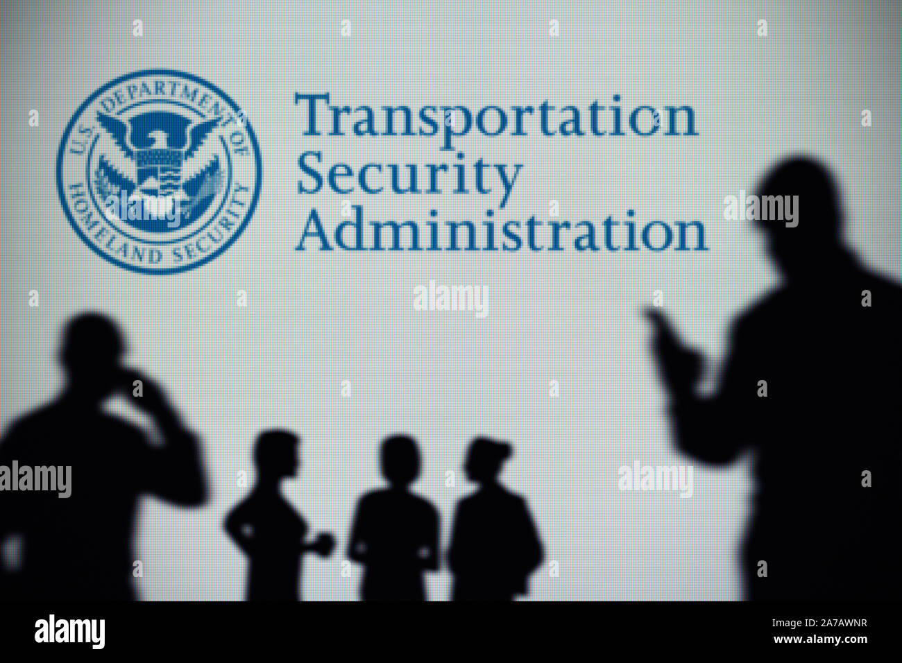 Transportation Security Administration logo is seen on a screen in the background while a silhouetted person uses a smartphone (Editorial use only). Stock Photo