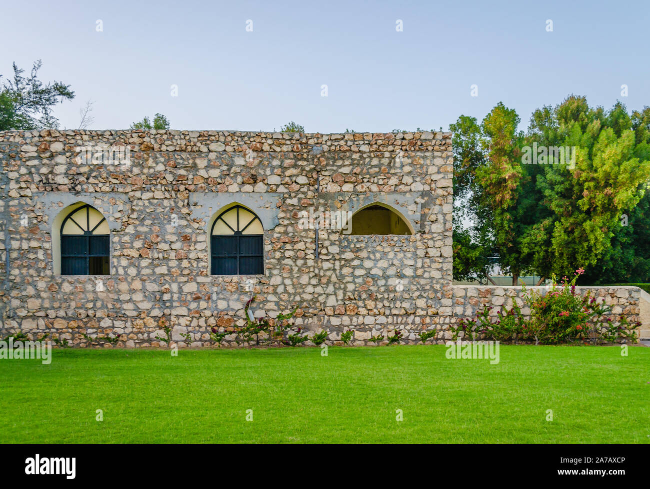 Old Fashioned Stone House with black window arches surrounded by plants and a green lawn in front. From Muscat, Oman. Stock Photo