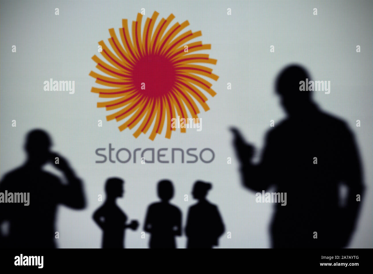 The Stora Enso logo is seen on an LED screen in the background while a silhouetted person uses a smartphone (Editorial use only) Stock Photo