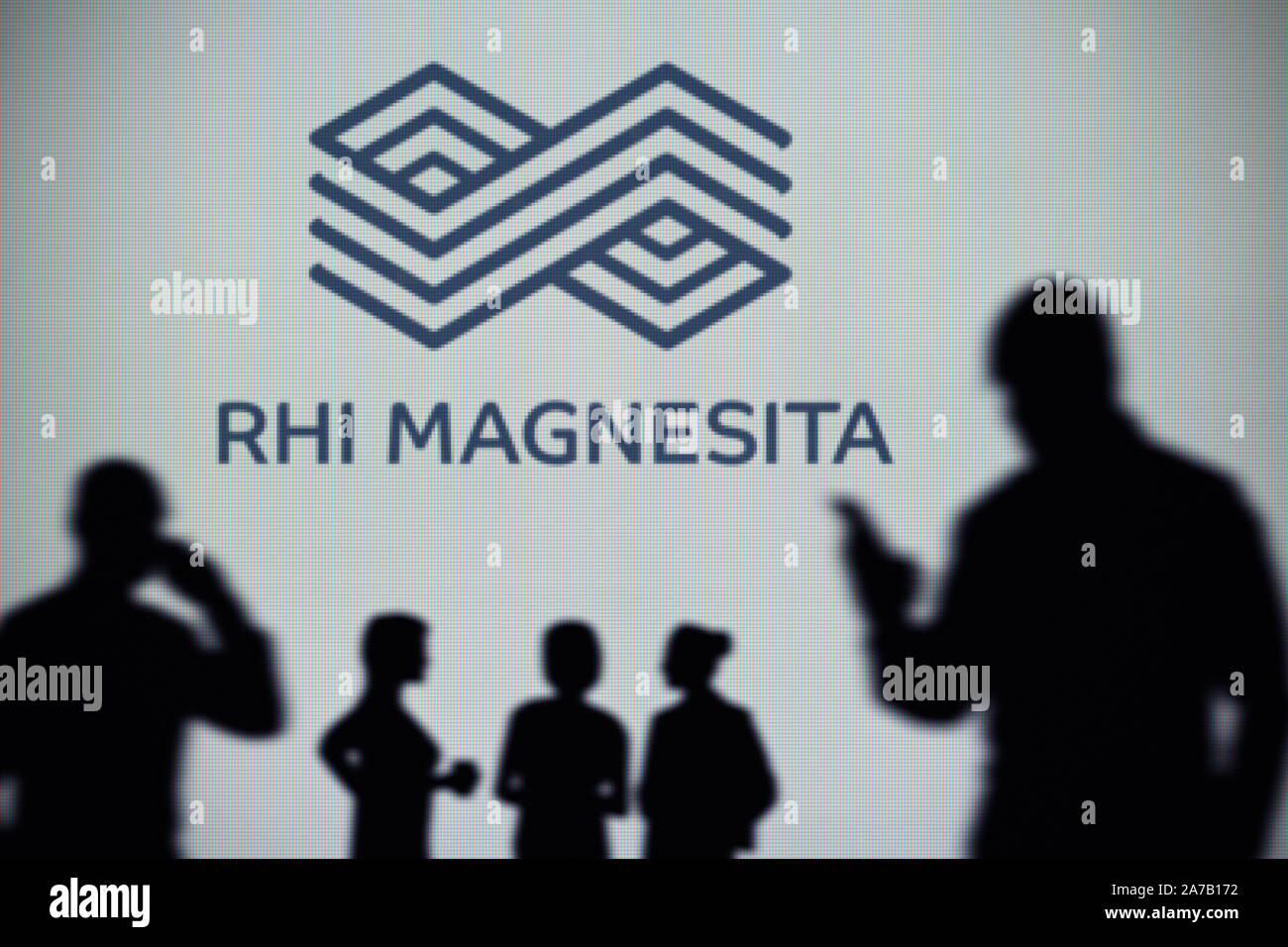 The RHI Magnesita logo is seen on an LED screen in the background while a silhouetted person uses a smartphone (Editorial use only) Stock Photo