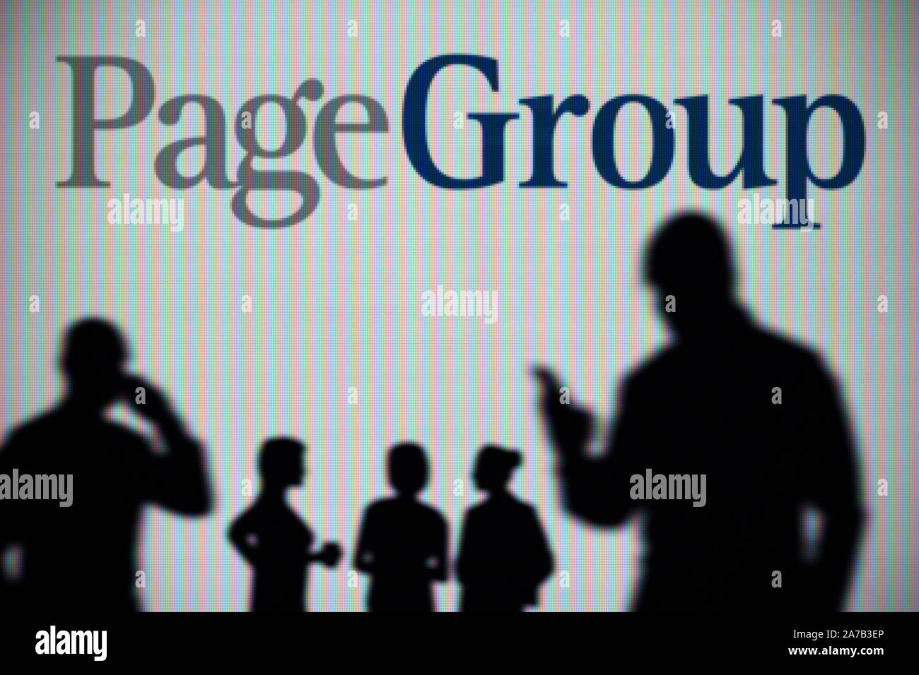 The PageGroup recruitment logo is seen on an LED screen in the background while a silhouetted person uses a smartphone (Editorial use only) Stock Photo