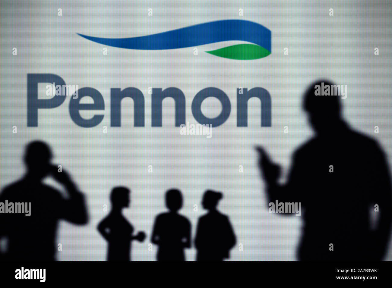 The Pennon Group logo is seen on an LED screen in the background while a silhouetted person uses a smartphone (Editorial use only) Stock Photo