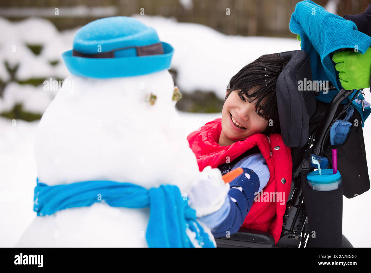 Happy smiling disabled boy in wheelchair placing a carrot on  a snowman Stock Photo