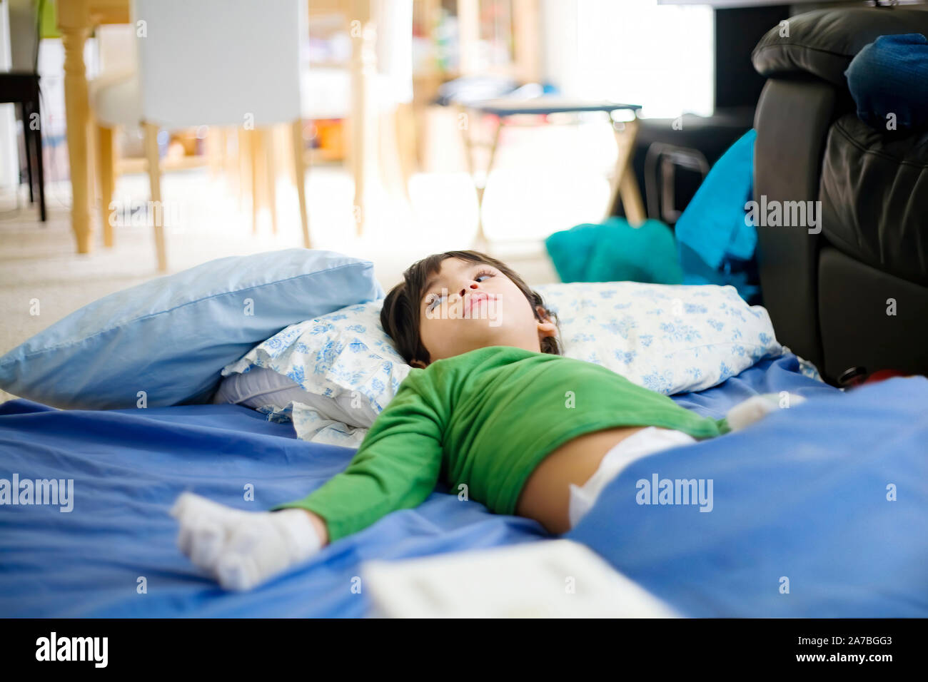 Young disabled boy with cerebral palsy lying on floor mat at home relaxing, wearing diapers Stock Photo