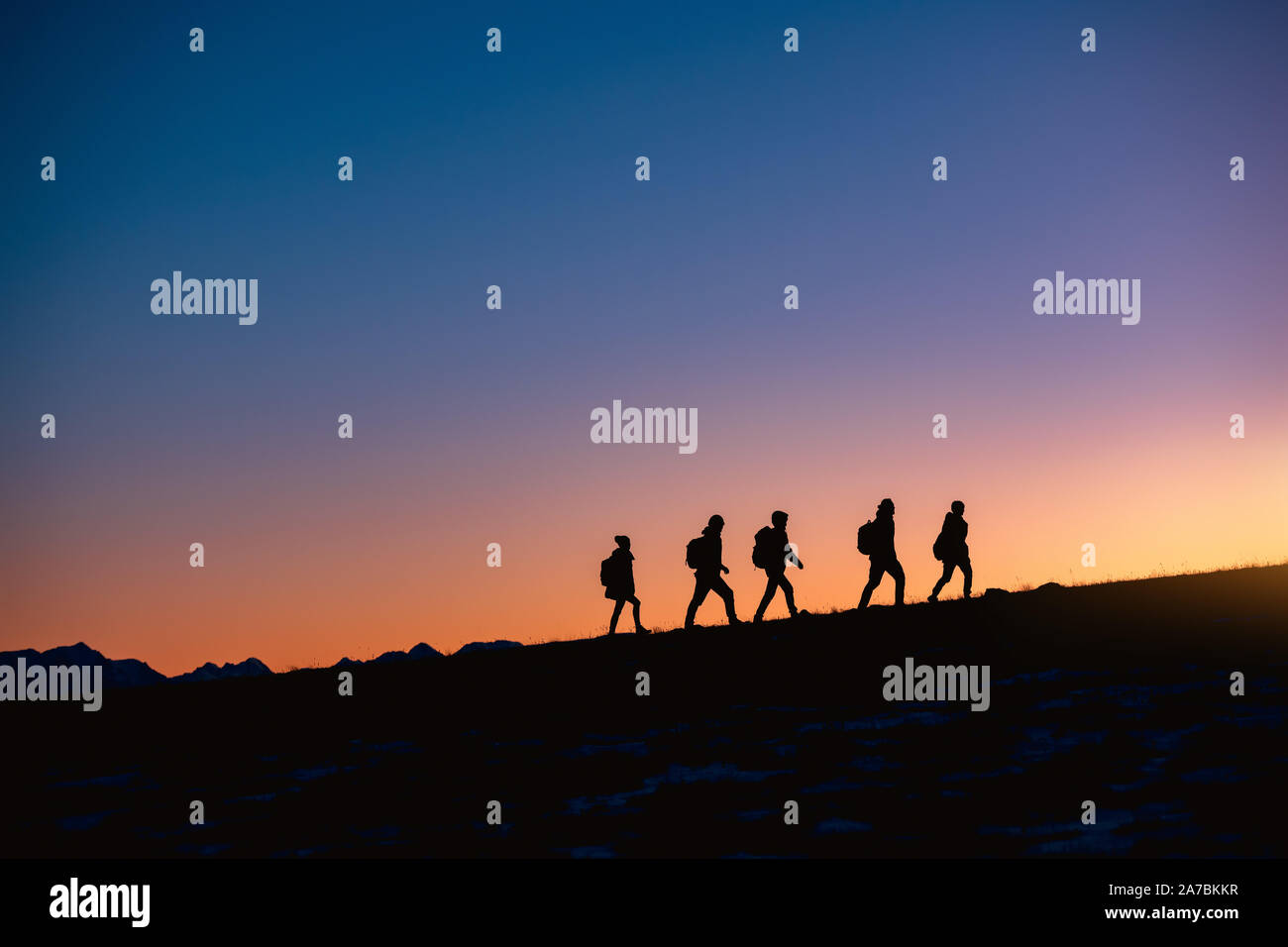 Silhouettes of group of hikers going uphill at sunset mountain Stock Photo