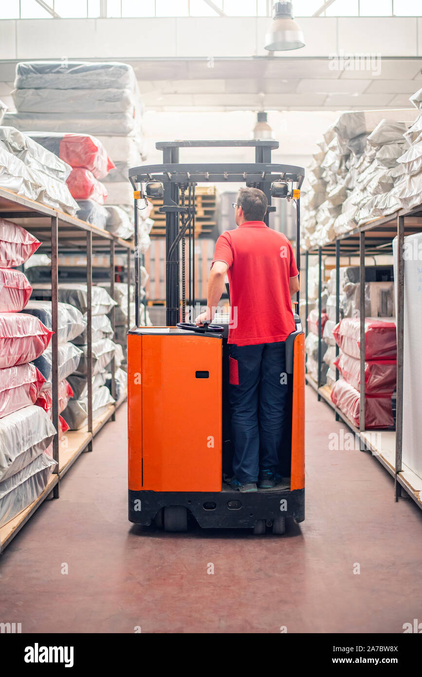 Warehouse clerk driving an electric stacker through warehouse aisles