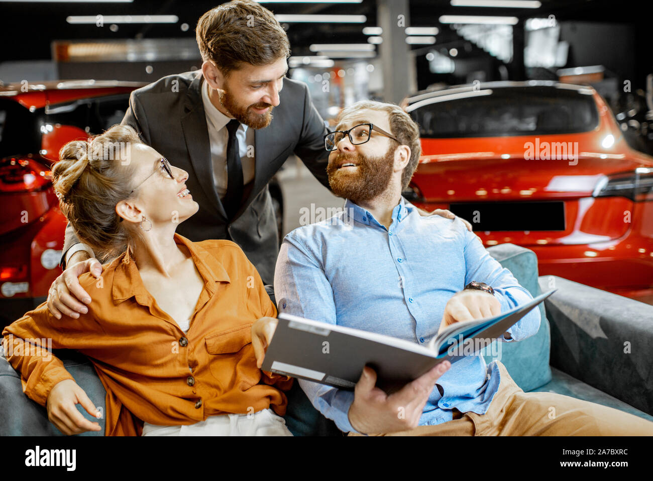 Young couple with annoying salesman choosing car finish using catalog