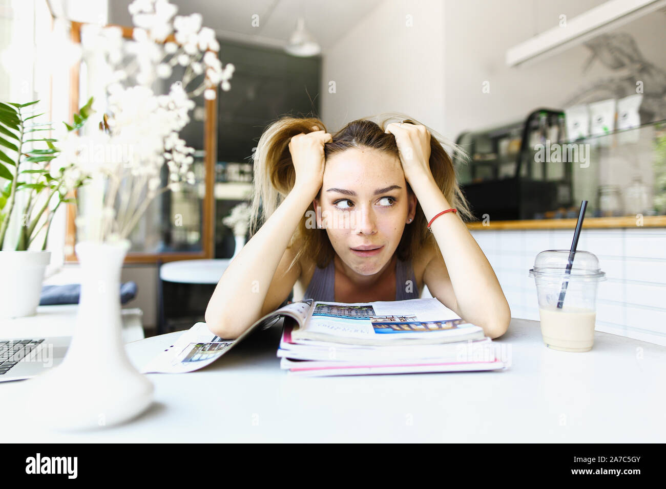 Tired female student sitting at cafe and reading notes. Stock Photo